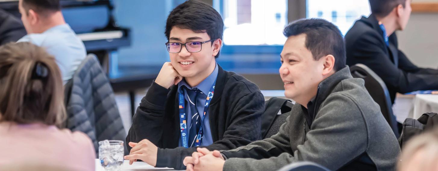 Male student in a tie sitting at a table with an adult