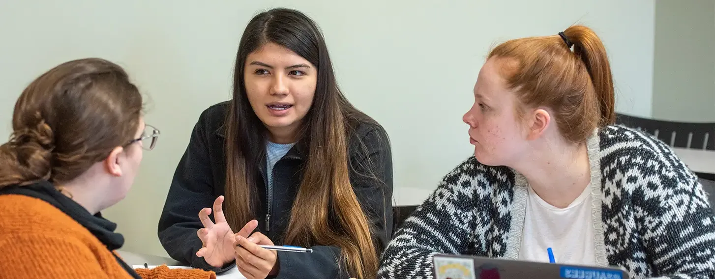 Three students engaged in a lively conversation while sitting at a table.